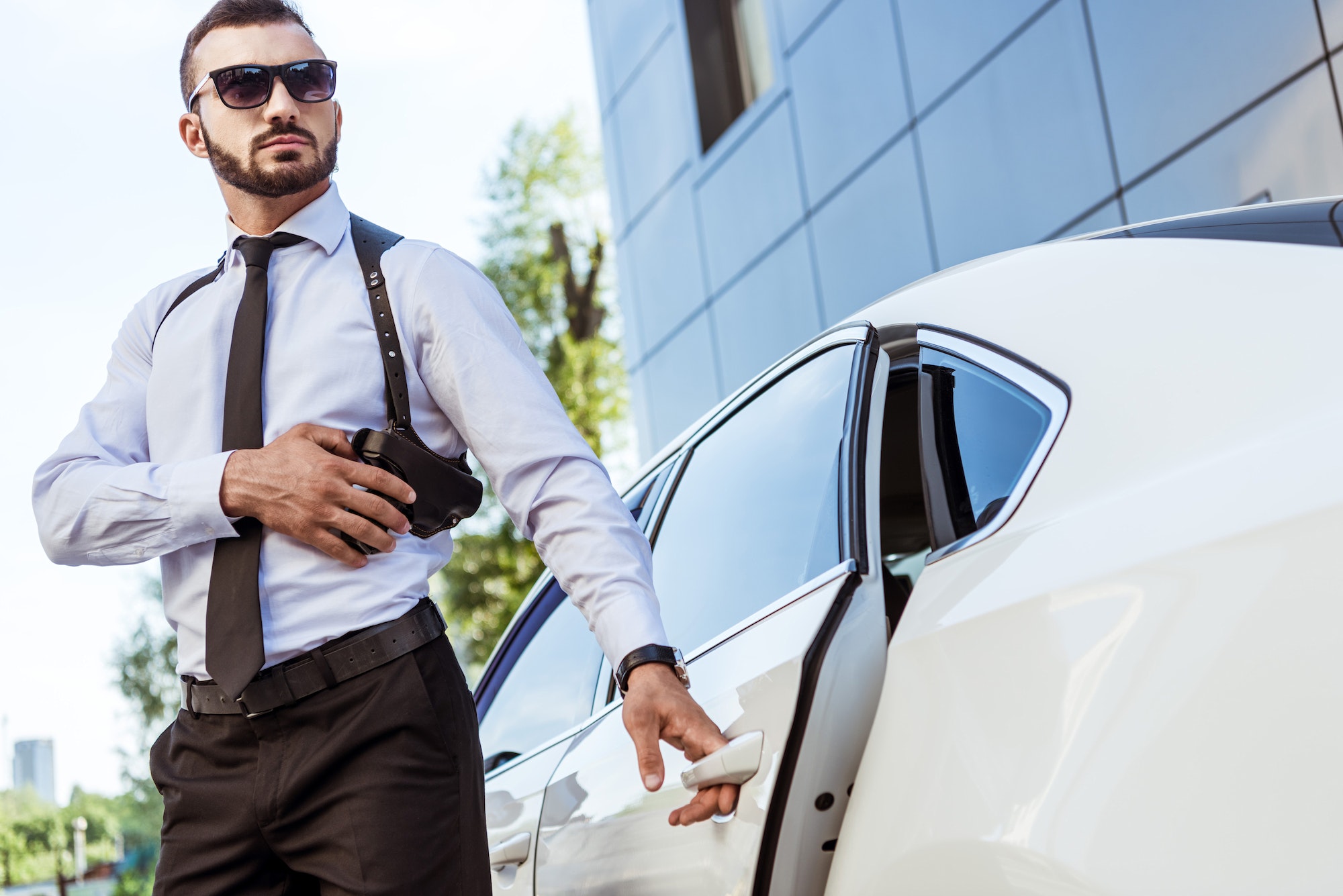 handsome bodyguard touching gun and opening car door