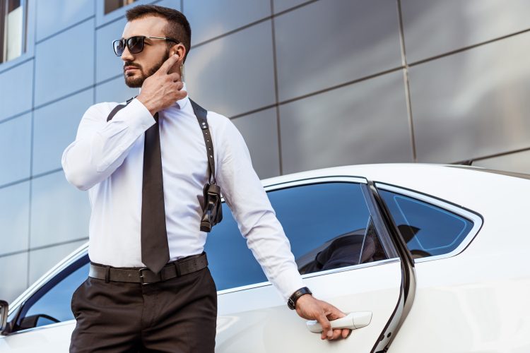 Handsome security guard listening message with security earpiece on street and opening car